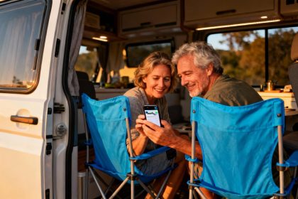 Couple d'âge mûr utilisant un smartphone avec l'application Park4Night dans leur camion aménagé au coucher du soleil