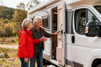 Couple âgé discutant avec un vendeur devant un camping-car rouge dans un camping ensoleillé
